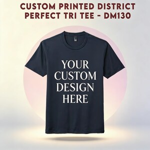 May include: A navy blue t-shirt with the text "YOUR CUSTOM DESIGN HERE" in white. The shirt is a Perfect Tri Tee, as indicated by the text at the top. The shirt has a crew neck and short sleeves.