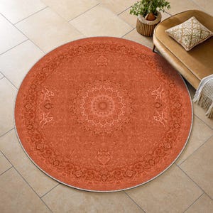 May include: A large, circular area rug in a vibrant burnt orange hue, featuring an intricate, symmetrical floral and medallion pattern in a darker shade of orange. The rug has a detailed border design and a clean, finished edge throughout.