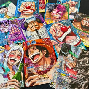 Op de afbeelding: Een verzameling kleurrijke ruilkaarten met anime-achtige illustraties van verschillende personages. Elke kaart toont namen van personages, speciale vaardigheden en het getal 5000. De kaarten zijn uit de "One Piece"-serie.