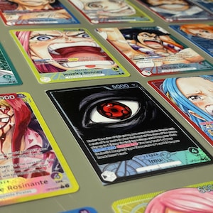 Può includere: Una collezione di carte collezionabili colorate con illustrazioni in stile anime. Le carte mostrano vari personaggi con opere d'arte vivaci e testo, tra cui il nome "Jewelry Bonney" e il numero "5000".