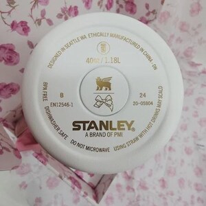 May include: White Stanley brand tumbler lid with gold accents. The lid features the Stanley logo, a lion emblem, and text indicating a 40 oz / 1.18L capacity. The lid is dishwasher safe and designed in Seattle, WA.