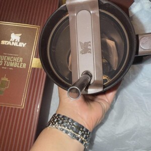 May include: A brown Stanley Quencher Flowstate 40 oz tumbler with a matching lid and straw. The tumbler is new in its original box, which features the Stanley logo and product information. The lid has a flip-top closure and a straw opening.