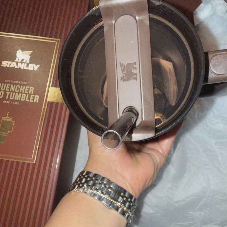 May include: A brown Stanley Quencher Flowstate 40 oz tumbler with a matching lid and straw. The tumbler is new in its original box, which features the Stanley logo and product information. The lid has a flip-top closure and a straw opening.