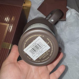 May include: A brown Stanley brand thermos with a handle and a screw-on lid. The bottom of the thermos has a white sticker with product information and a barcode. The thermos is dishwasher safe and BPA free.