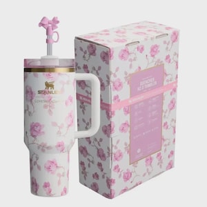 May include: A white Stanley Quencher H2.0 Tumbler with a pink rose pattern, a white handle, and a pink bow-shaped straw topper. The tumbler is next to its matching box, which also features the rose design.