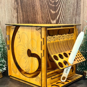 May include: A wooden craft organizer with a floral design cut into the side. The organizer has multiple compartments and slots for tools, including a Cricut tool. The wood has a light brown color.