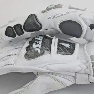 Op de afbeelding: Witte motorhandschoenen met zwarte en grijze accenten. De handschoenen hebben de tekst "3R DESIGN CONCEPT" en "FESE" erop staan. De handschoenen hebben een gewatteerd ontwerp en zijn gemaakt van leer.