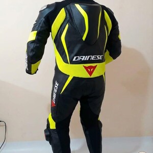K&ouml;nnte beinhalten: Schwarzer und gelber Motorrad-Rennanzug mit dem Logo "DAINESSE". Der Anzug hat gelbe Akzente an Schultern, R&uuml;cken und Beinen. Der Anzug h&auml;ngt an einem Kleiderb&uuml;gel.