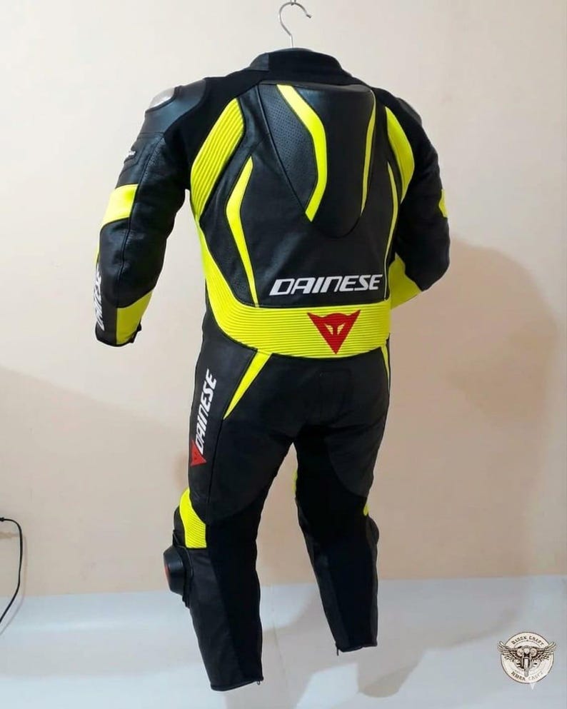 K&ouml;nnte beinhalten: Schwarzer und gelber Motorrad-Rennanzug mit dem Logo "DAINESSE". Der Anzug hat gelbe Akzente an Schultern, R&uuml;cken und Beinen. Der Anzug h&auml;ngt an einem Kleiderb&uuml;gel.
