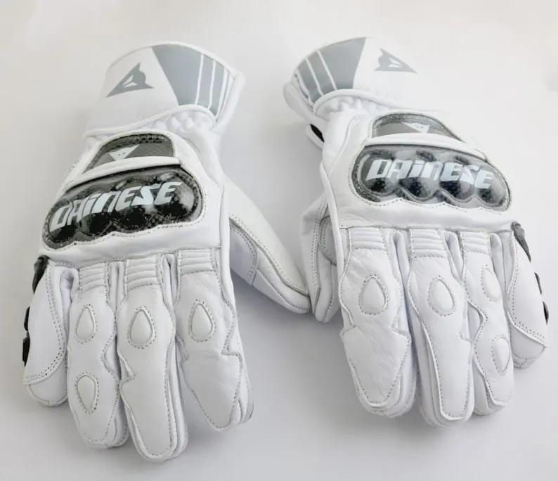 Op de afbeelding: Paar witte motorhandschoenen met de merknaam "Dainese" op de knokkels. De handschoenen hebben verstevigde padding op de handpalmen en vingers, met grijze accenten op de manchetten. Ontworpen voor bescherming en prestaties.