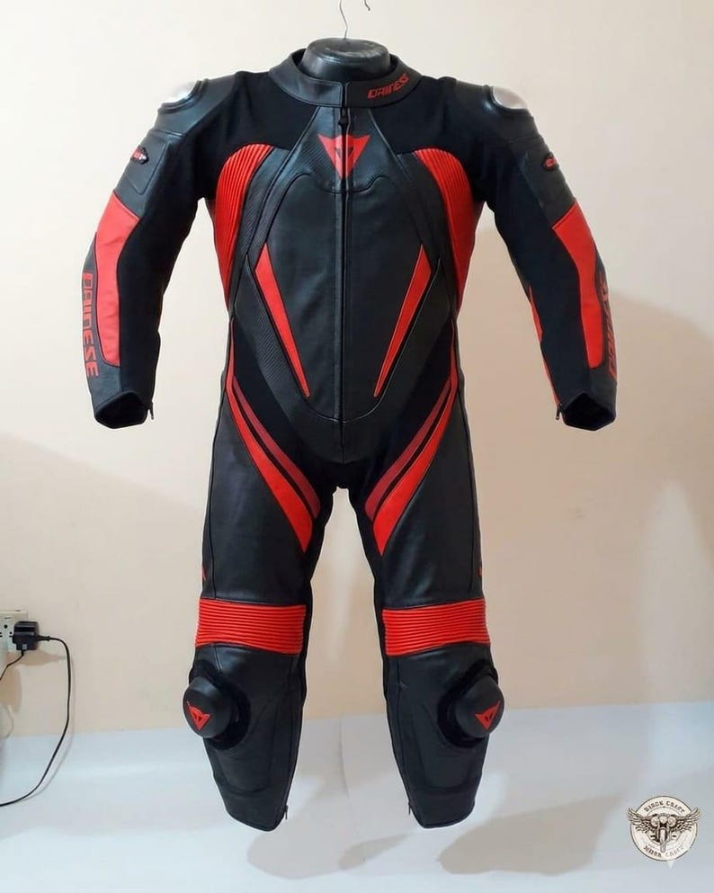 K&ouml;nnte beinhalten: Schwarzer und roter Motorrad-Rennanzug mit dem Markennamen "Dainese". Der Anzug hat rote Akzente an Armen, Beinen und Torso sowie Protektoren an Schultern und Knien.