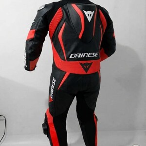 K&ouml;nnte beinhalten: Schwarzer und roter Motorrad-Rennanzug mit dem Markennamen "DAINESE". Der Anzug hat ein stromlinienf&ouml;rmiges Design mit roten Akzenten an Schultern, Armen und Beinen. Der Anzug h&auml;ngt an einem Kleiderb&uuml;gel.