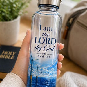 Puede incluir: Botella de agua de vidrio transparente con tapa y asa plateadas. La botella presenta el texto "I am the LORD thy God" y un gráfico azul y blanco de aerogeneradores. También es visible el texto "Isaías 43:3".