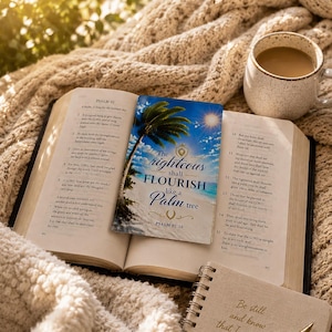 May include: An open Bible with a bookmark showing a palm tree and the words "The righteous shall flourish like a Palm tree." A small notebook with the text "Be still and know that I am God." is next to a gold pen. A cup of coffee is nearby.