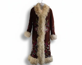 May include: A long brown coat featuring a thick cream-colored faux fur trim along the front opening, cuffs, and hem. The coat is decorated with colorful floral embroidery in shades of pink, blue, yellow, and green across the front and sleeves.