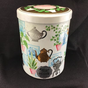 May include: A vintage white tin with a lid, decorated with illustrations of teapots, plants, and ships. The tin has a label that reads "Riley's Variety Toffee 15 OZ NET". The lid features a floral design.