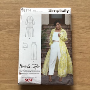 May include: A Simplicity sewing pattern package featuring a Mimi G Style design. The package includes illustrations of a long button-down dress, a camisole top, and pants. The package also shows a woman wearing a white outfit with a yellow patterned overcoat.