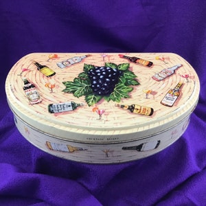 May include: Oval tin box with a woven basket design. The lid features illustrations of cocktail bottles, martini glasses, and a cluster of grapes. The words "COCKTAIL BASKET" are printed on the side of the box.