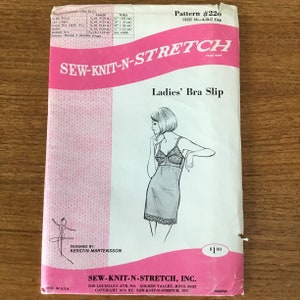 May include: A vintage sewing pattern for a Ladies' Bra Slip, size 32-A-B-C cup. The pattern packet is pink and white, with an illustration of the slip. The text on the packet includes "SEW-KNIT-N-STRETCH" and "Ladies' Bra Slip".