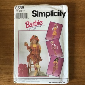 May include: Simplicity Barbie for girls sewing pattern. The pattern features a little girl in a plaid dress and hat, and illustrations of Barbie doll outfits. The pattern number is 8566, size BB (5-6X).