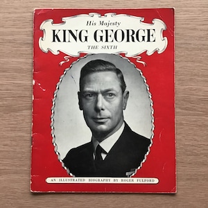 May include: A vintage book cover featuring a portrait of King George VI. The cover is red with white text that reads "His Majesty King George The Sixth." The book is an illustrated biography by Roger Fulford.
