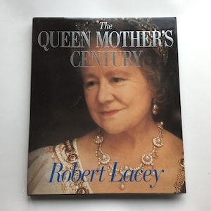 May include: A hardcover book titled "The Queen Mother's Century" by Robert Lacey. The cover features a portrait of the Queen Mother, with silver lettering and a dark background. The Queen Mother is wearing a pearl necklace and earrings.