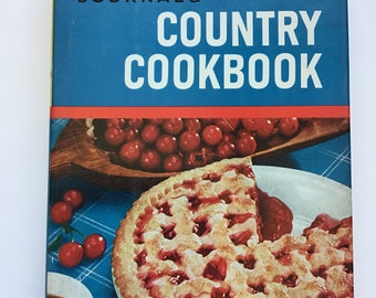 May include: A hardcover cookbook titled Farm Journal's Country Cookbook with the text More Than 1,000 Tested Recipes. The cover features a lattice-top cherry pie on a white plate, a wooden bowl filled with red cherries, and a cup of dark liquid.