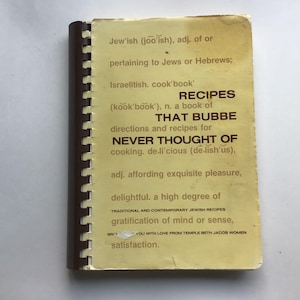 May include: A vintage cookbook titled "Recipes That Bubbe Never Thought Of," with a spiral binding. The cover is a faded yellow with black text, including the definition of "Jew'ish" and the phrase "Traditional and Contemporary Jewish Recipes."