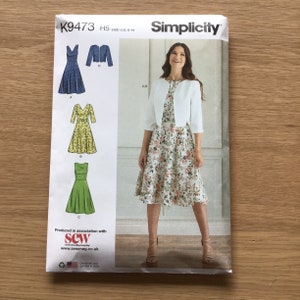 May include: Simplicity sewing pattern number K9473, size US 6-14, for a dress with a jacket. The pattern includes four different dress styles: a sleeveless dress with a scoop neck, a dress with a V-neck and 3/4 sleeves, a sleeveless dress with a scoop neck, and a dress with a V-neck and 3/4 sleeves. The jacket is a cropped style with a scoop neck and 3/4 sleeves.