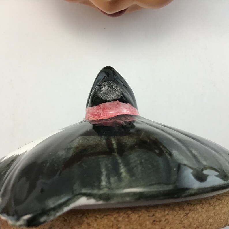 May include: Black and green ceramic lid with a pink band and a pointed top. The lid has a slight chip on the top.