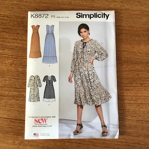 May include: Simplicity sewing pattern K8872, size U.S. 12-20, featuring four dress designs. The pattern includes a long-sleeved floral dress, a tiered dress, and two other dress styles. The package is printed in the USA.