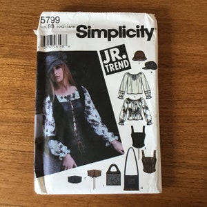 May include: Simplicity sewing pattern featuring a medieval-inspired design. The pattern includes options for a top, vest, hat, and bag. The package is white with the text "5799" and "JR. TREND" printed on it.