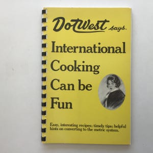 May include: A vintage cookbook with a yellow cover, black spiral binding, and the title "DotWest says... International Cooking Can be Fun." The cover features a portrait and text about recipes and tips for cooking.