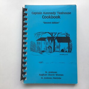Może przedstawiać: Niebieska okładka książki kucharskiej zatytułowanej "Captain Kennedy Teahouse Cookbook" z podtytułem "Second Edition". Okładka przedstawia czarno-białą ilustrację domu z drzewami i śniegiem. Na dole nadrukowany jest tekst "St. Andrews Anglican Church Women St. Andrews, Manitoba".