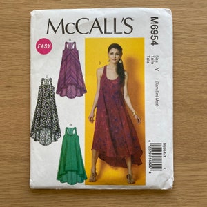 Pode incluir: Um envelope de padrão de costura McCall's com quatro designs de vestidos. Os designs incluem um padrão de chevron roxo, um vestido verde, uma estampa floral preta e um vestido estilo tie-dye vermelho. O padrão é rotulado como "Fácil" e inclui informações de tamanho.