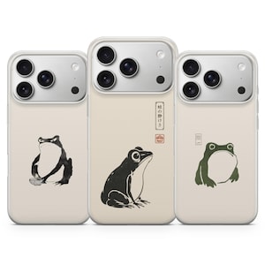 Puede incluir: Tres fundas de teléfono de color claro con ilustraciones de ranas. La funda izquierda muestra una rana en estilo de tinta negra, la central una rana negra con texto japonés y un sello rojo, y la derecha una rana verde con texto.