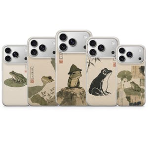 May include: Five smartphone cases featuring various artistic illustrations of frogs in a muted, earthy color palette. Each case displays a unique frog design, including frogs on lily pads, rocks, and bamboo, with Japanese text and red seal stamps.