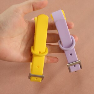 May include: Two silicone collars, one bright yellow and one light lavender, each featuring a matching sliding loop, a fixed D-ring, multiple adjustment holes, and a silver-toned metal buckle for secure fastening and adjustable sizing.