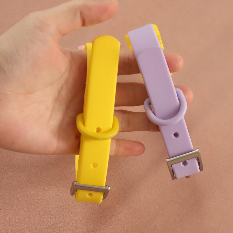 May include: Two silicone collars, one bright yellow and one light lavender, each featuring a matching sliding loop, a fixed D-ring, multiple adjustment holes, and a silver-toned metal buckle for secure fastening and adjustable sizing.