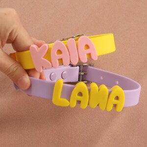 May include: Two silicone collars with metal buckles. The yellow collar features the name KAIA in pink letters, while the lavender collar displays the name LANA in yellow letters. Both collars have adjustable holes and a smooth, matte finish.