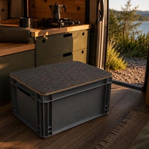 Könnte beinhalten: Eine graue Kunststoff-Aufbewahrungsbox mit Filzoberfläche in einem Wohnmobil. Die Kiste hat einen Holzrahmen und das Wort "PLYVAN" ist auf der Seite aufgedruckt. Ein Edelstahlbecher und eine schwarze Wasserflasche sind ebenfalls sichtbar.