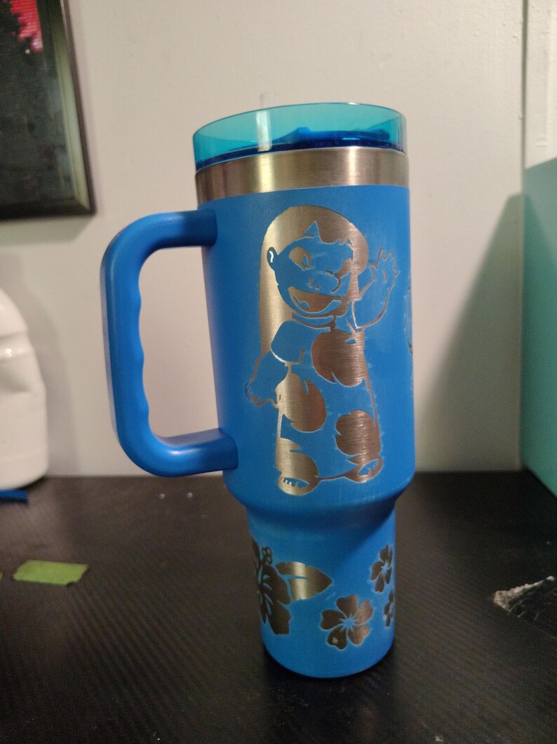 Peut inclure: Un gobelet bleu en acier inoxydable avec une poign&eacute;e et un couvercle bleu translucide. Le gobelet pr&eacute;sente un motif grav&eacute; au laser d'un personnage de dessin anim&eacute; aux grandes oreilles et un motif floral sur la partie inf&eacute;rieure en m&eacute;tal argent&eacute;.