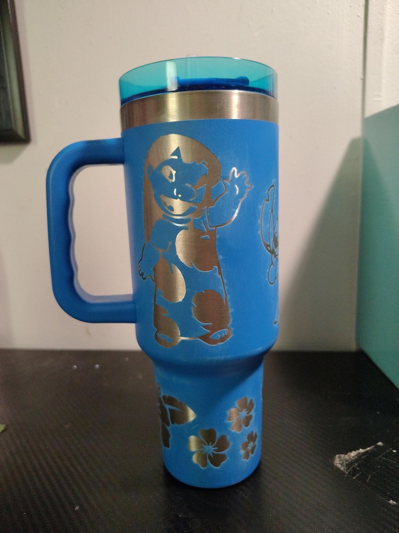 Peut inclure: Un gobelet isotherme bleu vif avec une poign&eacute;e et un couvercle bleu translucide. L'ext&eacute;rieur pr&eacute;sente un motif grav&eacute; au laser d'un personnage de dessin anim&eacute; en robe &agrave; motifs faisant signe, ainsi que des motifs floraux grav&eacute;s pr&egrave;s de la base.
