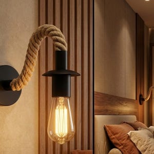 May include: A black wall sconce with a rope-wrapped arm and a vintage-style lightbulb. The sconce is mounted on a wall with a wooden panel design, creating a rustic and industrial aesthetic. The lightbulb emits a warm, inviting glow.