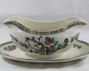 May include: A white porcelain gravy boat with a floral pattern and gold trim. The boat is on a matching saucer.