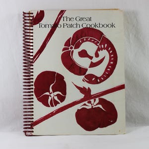 May include: A white spiral bound cookbook with a red design on the cover. The title of the book is "The Great Tomato Patch Cookbook".
