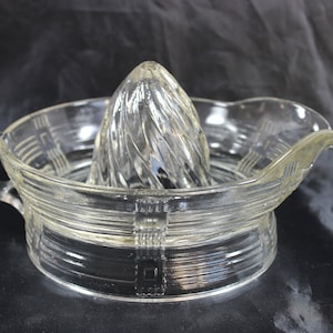May include: A clear glass citrus juicer with a ribbed design. The juicer has a handle and a spout for pouring.