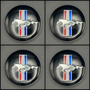Puede incluir: Cuatro emblemas circulares negros con un logotipo plateado de un caballo corriendo y rayas verticales rojas, blancas y azules. Los emblemas tienen un acabado brillante y están dispuestos en una cuadrícula de 2x2.