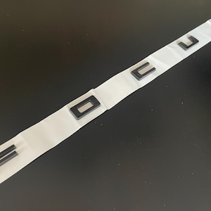 Könnte beinhalten: Schwarze Kunststoffbuchstaben, die "FOCUS" auf einem weißen Klebestreifen buchstabieren. Die Buchstaben sind in einer fetten, serifenlosen Schriftart gehalten. Der Streifen ist gefaltet und liegt auf einer dunklen Oberfläche.