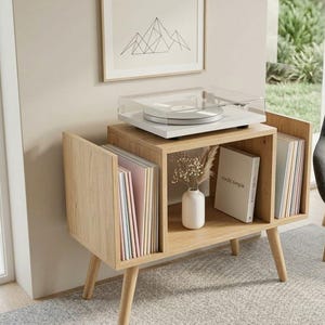 May include: A light wood record player stand with a white turntable and a framed mountain art print. The stand has open storage for records and a small vase with dried flowers. The stand is 76 cm wide.